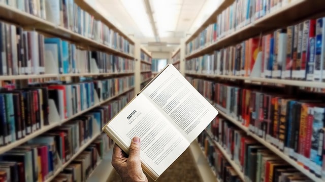 photo of hand holding a book in the middle of a library