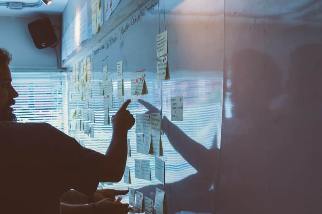 person pointing at sticky note paper on whiteboard wall