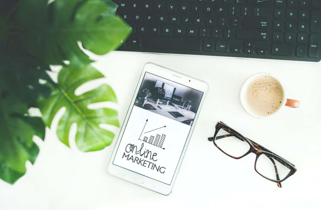 a tablet with a background photo that says "online marketing", with a keyboard, cup of coffee, and pair of glasses