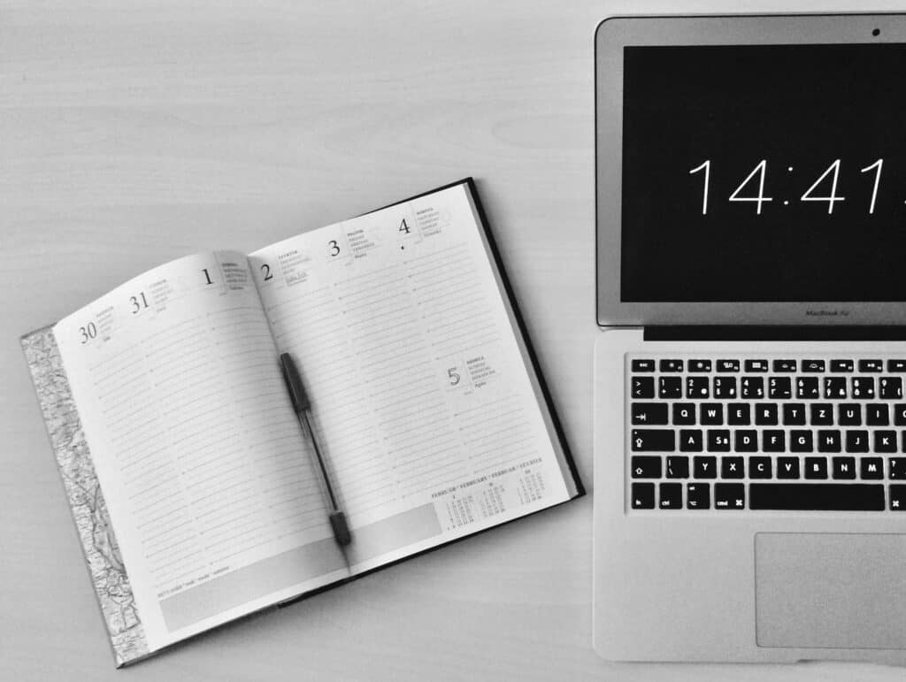 an open writing notebook and a computer showing 14:41