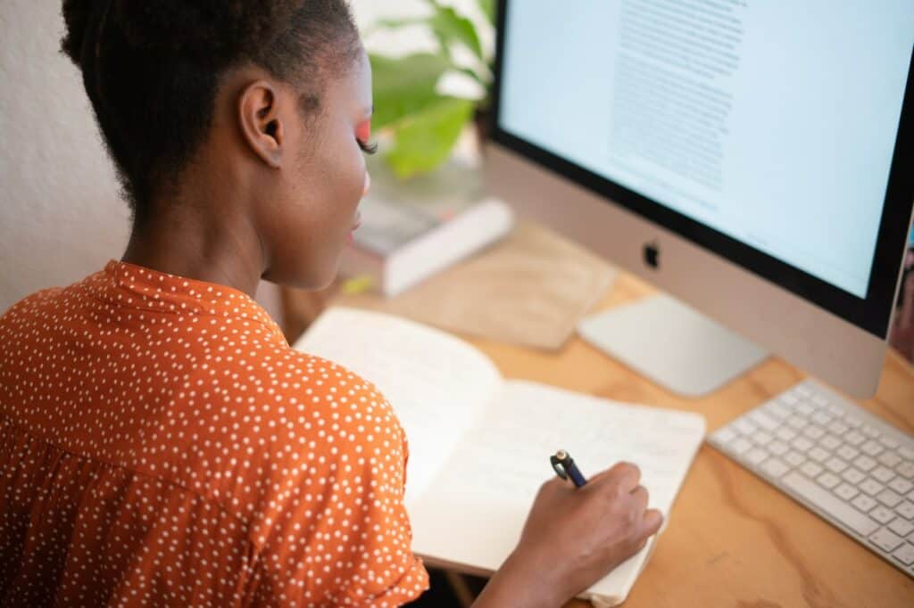 woman writing on a notebook in front of a computer